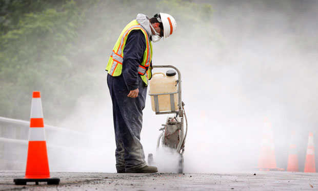 A transportation worker creates a dust cloud while cutting concrete