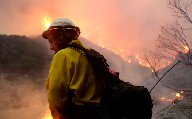 A wildlands firefighter stands in front of a wildfire