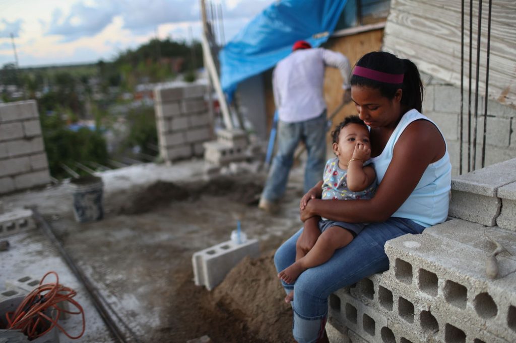 A mother holds her baby as her husband works to reconstruct their home destroyed by Hurricane Maria in San Isidro, Puerto Rico, on December 23, 2017.