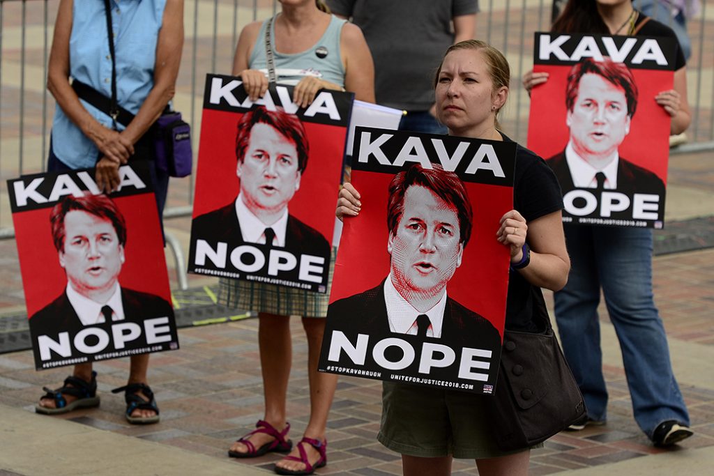 A woman holds up a sign during a rally to protest President Donald Trump's Supreme Court justice nominee Brett Kavanaugh, Denver, August 2018.