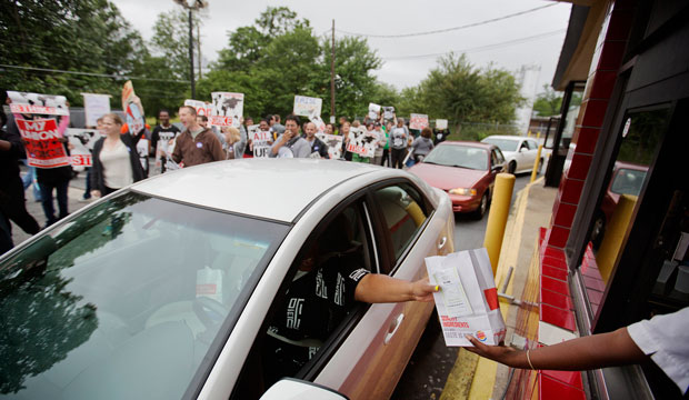 A worker hands a food order over to a customer as demonstrators march through a Burger King restaurant drive-thru in Atlanta, Georgia, protesting for higher wages and a worker's union.